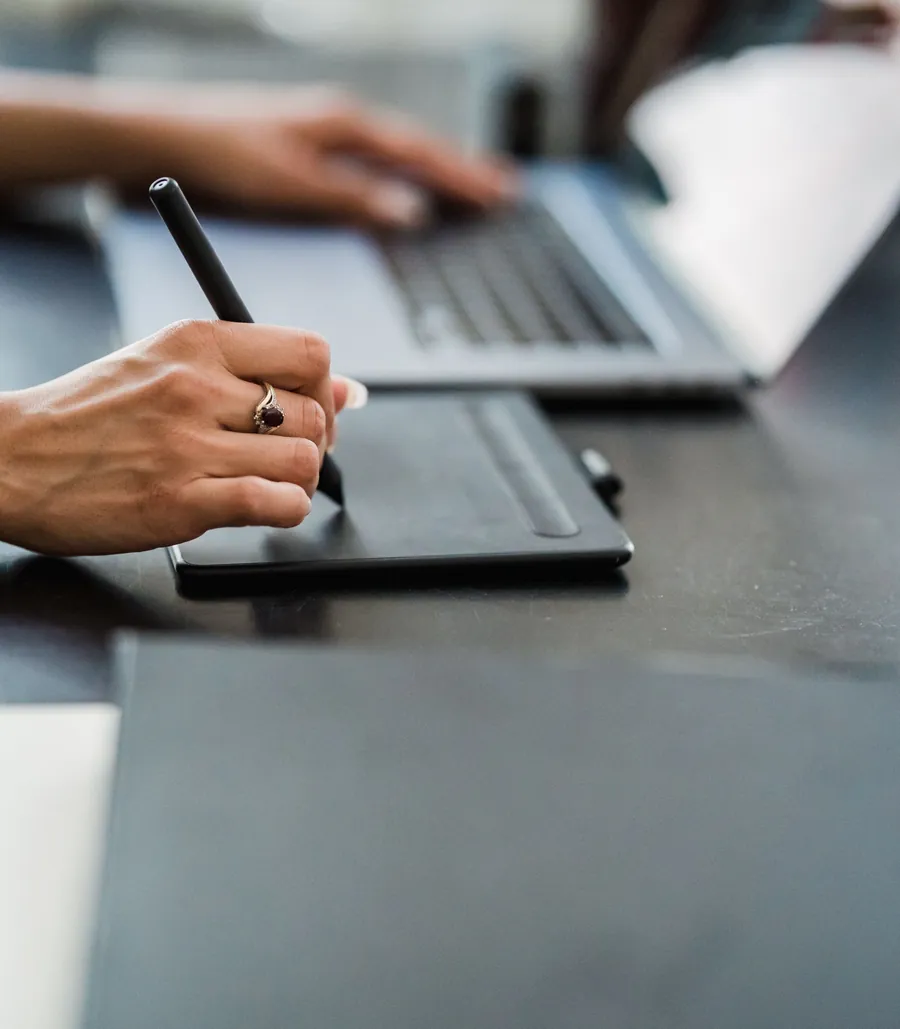 Close-up of a person working at a laptop with a pen tablet on a dark desk
